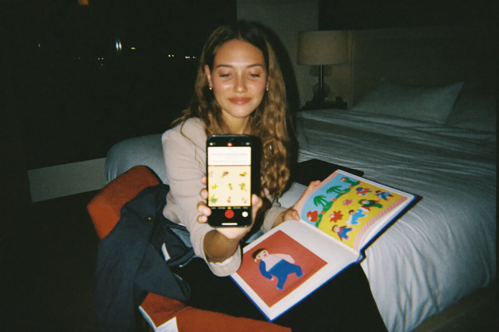 A father reading a picture book aloud toward his phone in a hotel room at night